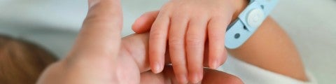 Nyfödd hand håller i förälders finger
