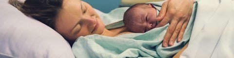 Kvinna på förlossningen med sin nyfödda bebis på magen